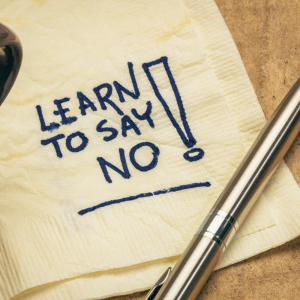 A close-up of a coffee cup next to a pen and a napkin with "LEARN TO SAY NO!" written on it.