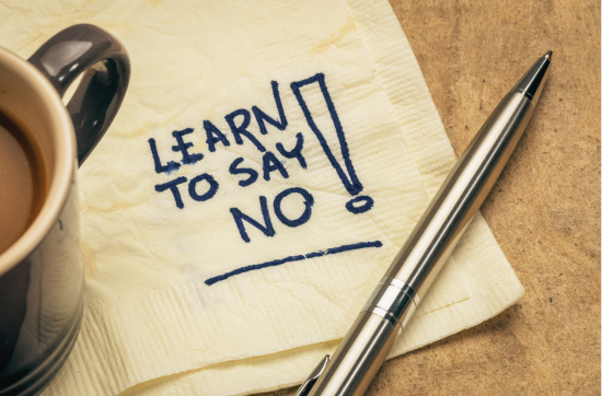 A close-up of a coffee cup next to a pen and a napkin with "LEARN TO SAY NO!" written on it.